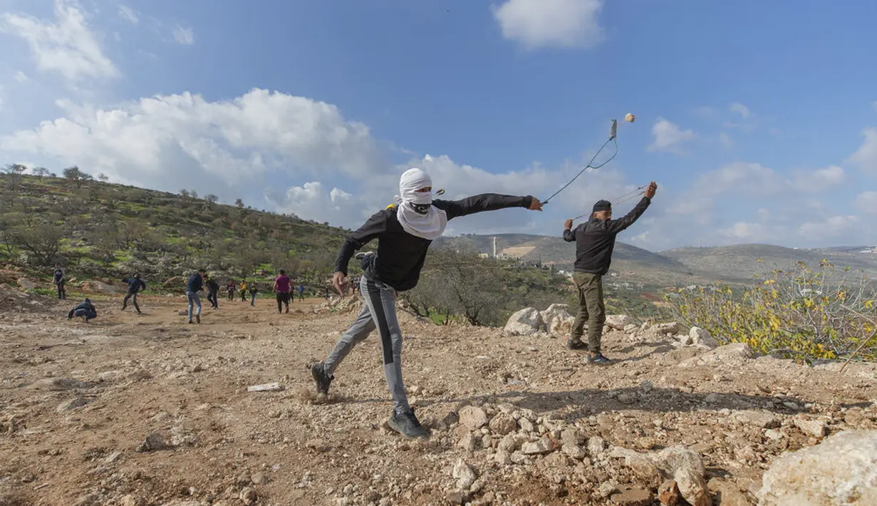 Pengunjuk rasa Palestina menggunakan ketapel saat bentrok melawan tentara Israel di Desa Mughayer, Ramallah, Tepi Barat, Jumat (18/12/2020). Pengunjuk rasa Palestina yang menggunakan ketapel terlibat bentrok dengan pemukim Yahudi yang menggunakan anjing. (AP Photo/Nasser Nasser)