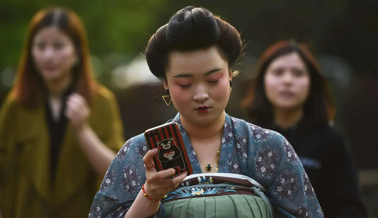 Seorang wanita bermain ponsel saat mengenakan kostum Dinasti Tang di Danau Barat di Hangzhou di provinsi Zhejiang timur China (31/3). Bahan pakaian Dinasti Tang terbuat dari sutra dan terkenal karena kelembutan dan ringan.  (AFP Photo/China Out)