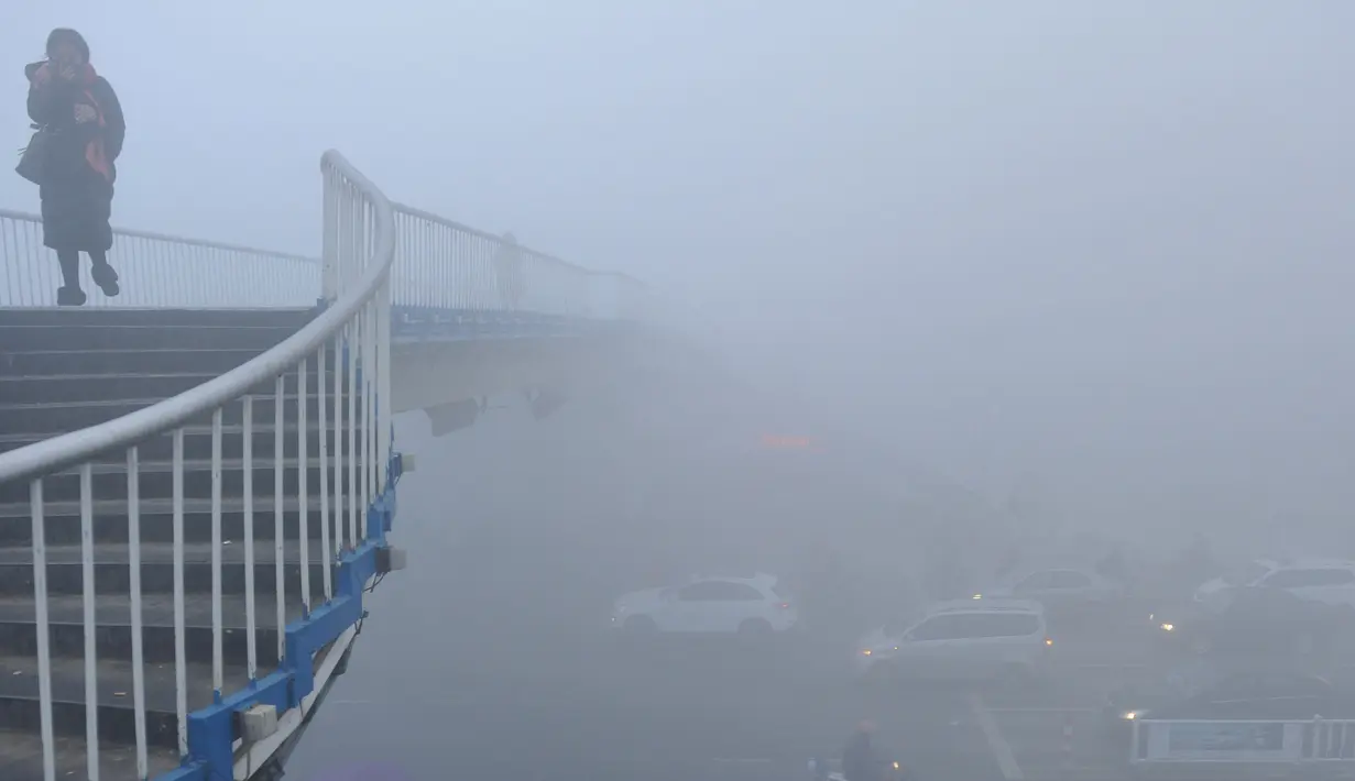 Warga berjalan melewati jembatan dengan kabut tebal akibat polusi udara yang kurang baik di Fuyang, Provinsi Anhui, China, (3/1). Kabut tebal ini membuat sejumlah warga mengunakan masker saat beraktivitas. (China Daily/via Reuters)