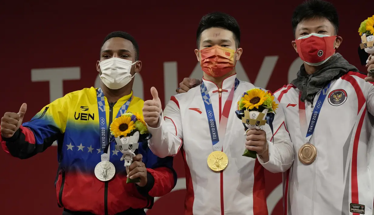 Peraih medali emas Shi Zhiyong dari China (tengah) diapit peraih medali perak Julio Ruben Mayora Pernia dari Venezuela (kiri) dan peraih medali perunggu Rahmat Erwin Abdullah dari Indonesia di podium cabang angkat besi 73 kg putra Olimpiade Tokyo 2020, Jepang, Rabu (28/7/2021). (AP Photo/Luca Bruno)