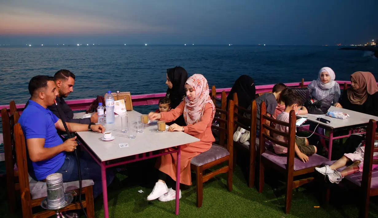 Keluarga Palestina menikmati makanan di sebuah restoran di sepanjang pantai di Kota Gaza (10/6/2019). Pergi ke restoran di dekat pantai merupakan opsi bagi warga Palestina untuk menikmati suasana alam. (AFP Photo/Mohammed Abed)