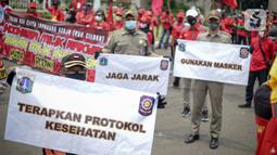 Petugas Satpol PP memegang poster imbauan protokol kesehatan COVID-19 saat unjuk rasa buruh di depan Gedung DPR, Jakarta, Selasa (17/11/2020). Pemerintah terus mengingatkan pentingnya 3M yaitu memakai masker, menjaga jarak, dan mencuci sebagai upaya pencegahan Covid-19. (Liputan6.com/Faizal Fanani)