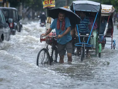 Seorang pria membawa tabung gas di sepedanya dan menyeberangi jalan yang banjir saat hujan deras di Guwahati, negara bagian Assam, India, Kamis (16/6/2022). Pemerintah Assam telah memerintahkan penutupan semua institusi pendidikan di Guwahati karena peringatan siaga merah untuk hujan lebat. (AP Photo/Anupam Nath)