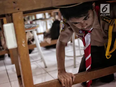 Sejumlah siswa berlindung di bawah meja saat simulasi bencana di SMA Negeri 78 Jakarta, Rabu (23/1). Kegiatan itu untuk pengenalan kepada siswa-siswi dengan program siaga bencana berupa simulasi evakuasi gempa dan tsunami. (Liputan6.com/Faizal Fanani)