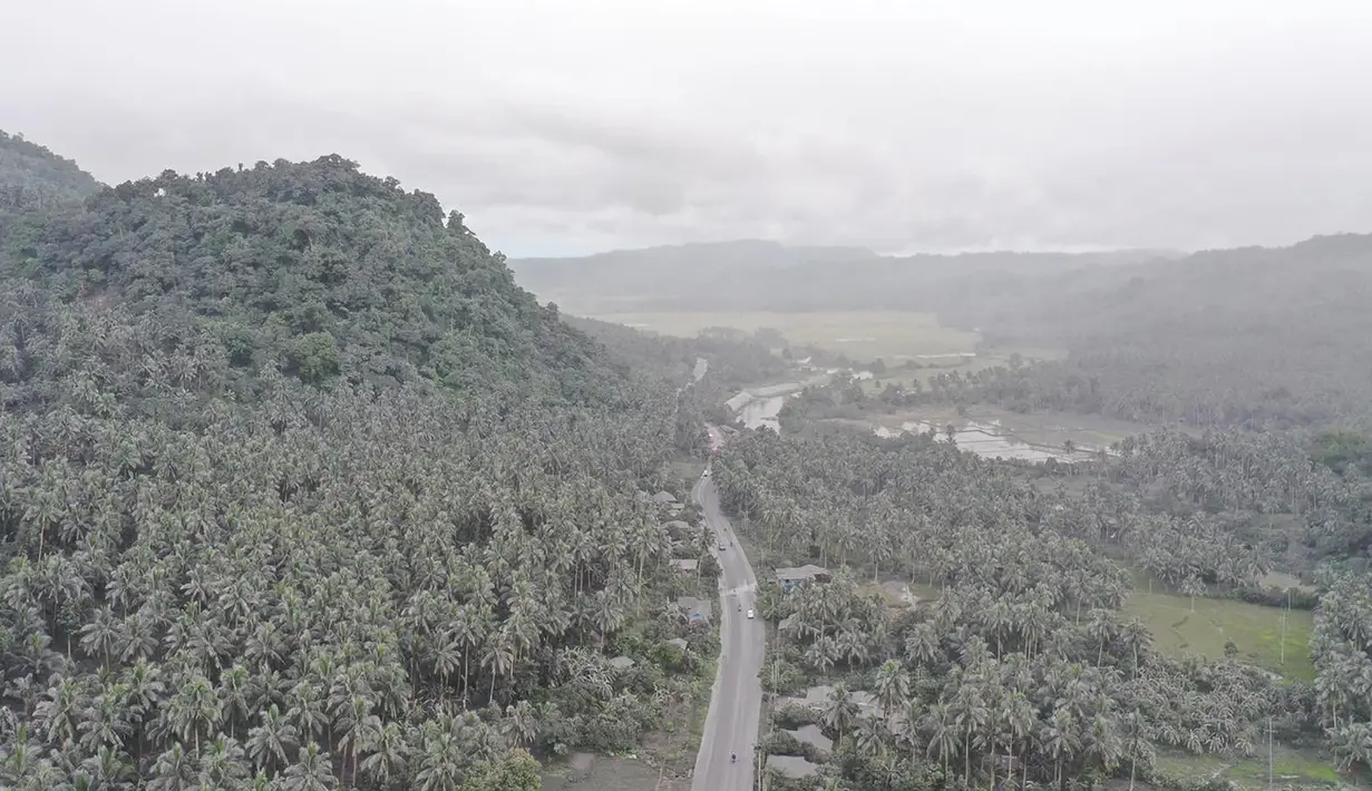 Foto selebaran yang diambil dan dirilis pada 5 Juni 2022 menunjukkan kendaraan melaju melewati rumah-rumah dan vegetasi yang tertutup abu di kota Juban, provinsi Sorsogon, Filipina, setelah gunung berapi Bulusan meletus dan mengirimkan gumpalan abu ke daerah tersebut. (Handout / Sorsogon Provincial Public Information Office / AFP)