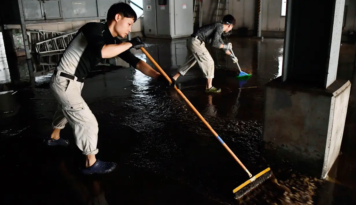Pekerja membersihkan area parkir setelah bangunan perusahaan mereka terkena banjir menyusul topan Hagibis di Kawasaki, Minggu (13/10/2019).  Topan Hagibis akhir pekan ini  disebut sebagai badai terburuk sejak 60 tahun terakhir yang pernah melanda Jepang. (Kyodo News via AP)