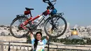 Pria Taiwan, Jacky Chen (40), berpose mengangkat sepedanya di Bukit Zaitun yang menghadap ke Kota Tua Yerusalem dan Kubah Batu pada 10 Juni 2019. Mantan teknisi elektronik itu berhenti dari pekerjaannya demi mewujudkan impiannya berkeliling dunia dengan sepeda. (MENAHEM KAHANA/AFP)