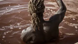 Toure, pemanen garam Gambia, melakukan manuver di samping kapalnya di Danau Retba (Danau Merah Muda) di Senegal pada 16 Maret 2021. Warna pink yang mencolok disebabkan oleh bakteri Dunaliella salina, yang tertarik dengan kadar garam yang dimiliki Retba. (MARCO LONGARI/AFP)