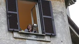 Seorang wanita bermain panci dari jendela rumah mereka selama flash mob di lingkungan Roma, Jumat (13/3/2020).  Lebih dari 23.000 orang berpartisipasi dalam flash mob untuk memainkan instrumen dan bernyanyi di tengah darurat virus corona Covid-19. (Cecilia Fabiano/LaPresse via AP)