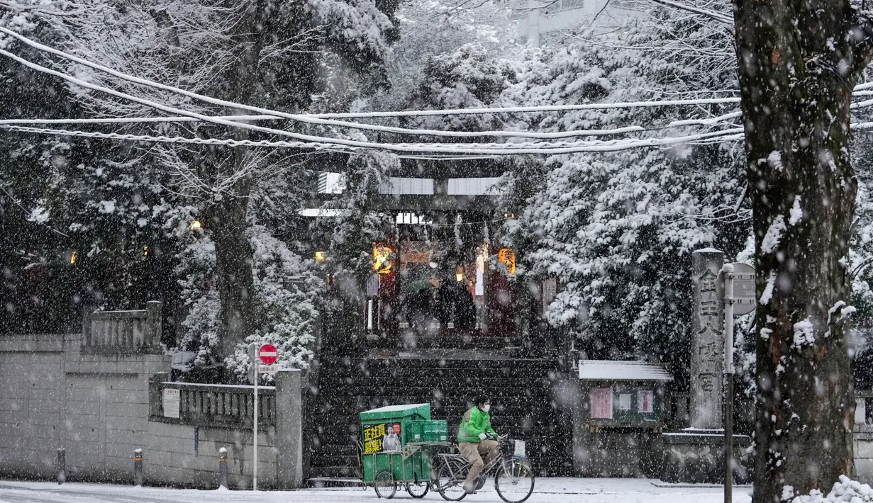 Seorang pekerja layanan pengiriman mengendarai sepeda melewati kuil Shinto saat salju turun di Tokyo, Kamis (6/1/2022). Pusat Tokyo dan kota Tsukuba, Prefektur Ibaraki, mencatat 3 sentimeter salju, sementara Chiba dan Yokohama memiliki 2 cm salju. (AP Photo/Kiichiro Sato)
