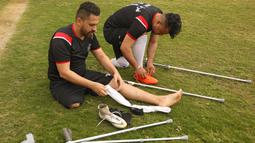 Dua pemain klub Al-Jazeera memakai perlengkapan menjelang pertandingan final kejuaraan lokal sepak bola korban amputasi melawan Al-Abtal yang diselenggarakan oleh Komite Palang Merah Internasional (ICRC), di tengah pandemi COVID-19, di Kota Gaza, Palestina, (18/3/2021). (AFP/Mohammed Abed)