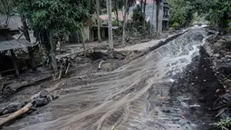 Air di jalan mengalir melewati rumah-rumah yang rusak di Dusun Kamar Kajang, Lumajang, Kamis (9/12/2021). Puluhan rumah terendam luapan air sungai bercampur material lahar dingin erupsi Gunung Semeru akibat diguyur hujan deras pada Selasa (7/12) dan Rabu (8/12) malam. (Juni Kriswanto/AFP)