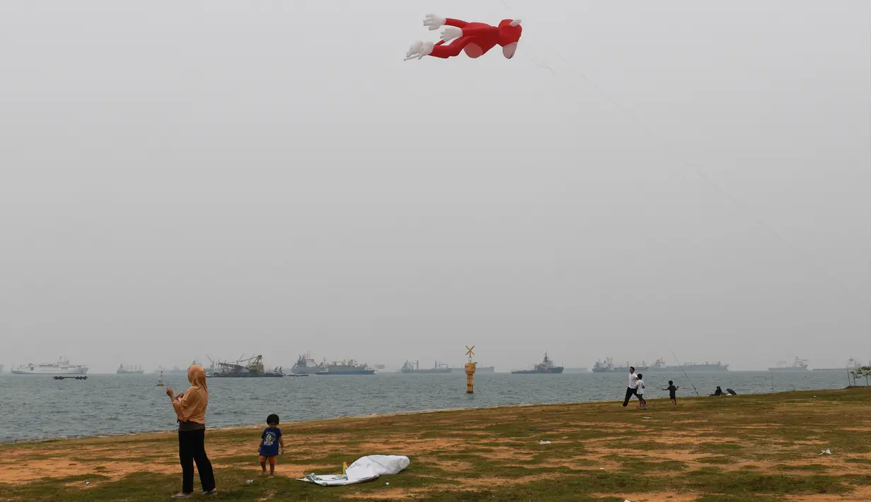 Warga menerbangkan layang-layang saat kabut asap menyelimuti kota Singapura (15/9/2019). Polusi dari kebakaran hutan di Indonesia mendorong kualitas udara Singapura ke tingkat yang tidak sehat untuk pertama kalinya dalam tiga tahun. (AFP Photo/Roslan Rahman)