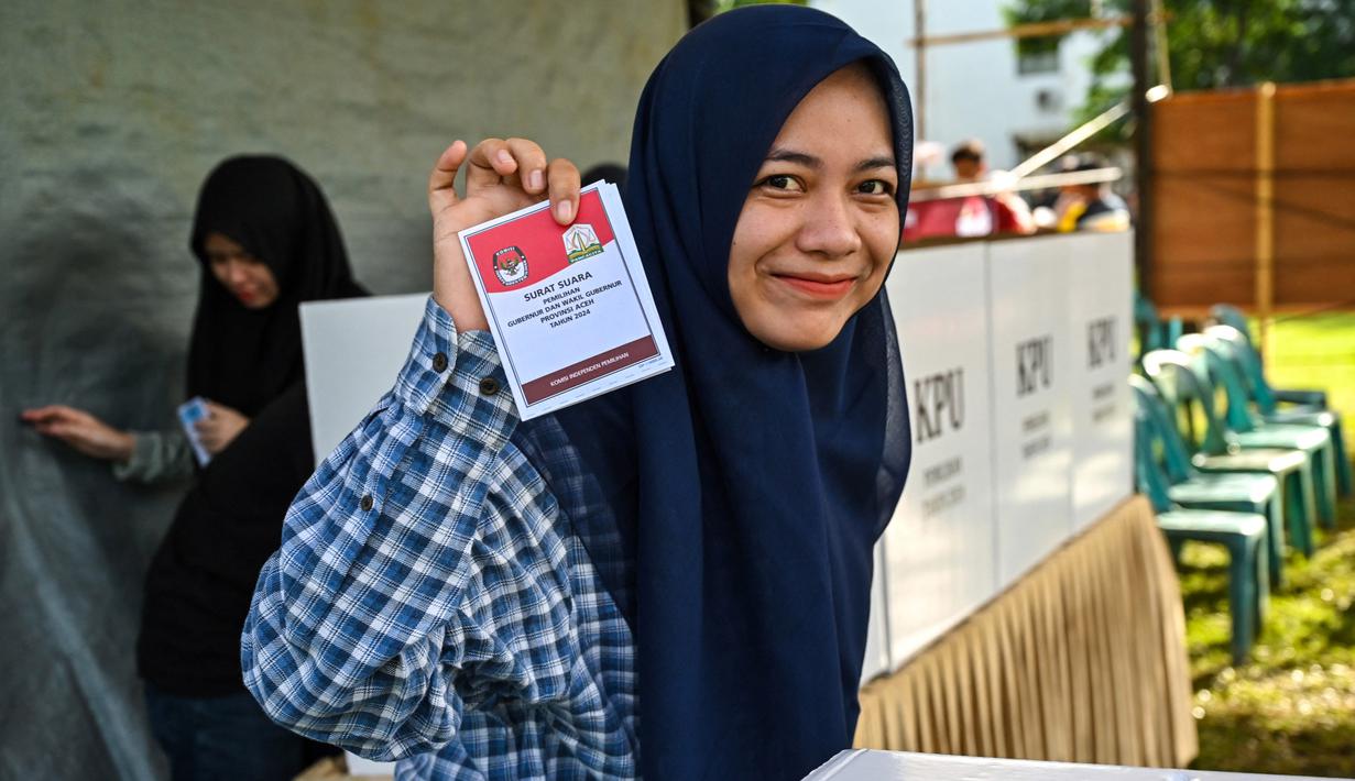 Hari ini, Rabu 27 November 2024, masyarakat Indonesia menggunakan hak politiknya untuk memilih pemimpin daerah dalam Pilkada Serentak 2024. Tampak dalam foto, seorang perempuan menunjukkan kertas suara saat pemilihan kepala daerah di Darul Imarah, pinggiran Banda Aceh, pada 27 November 2024. (CHAIDEER MAHYUDDIN/AFP)