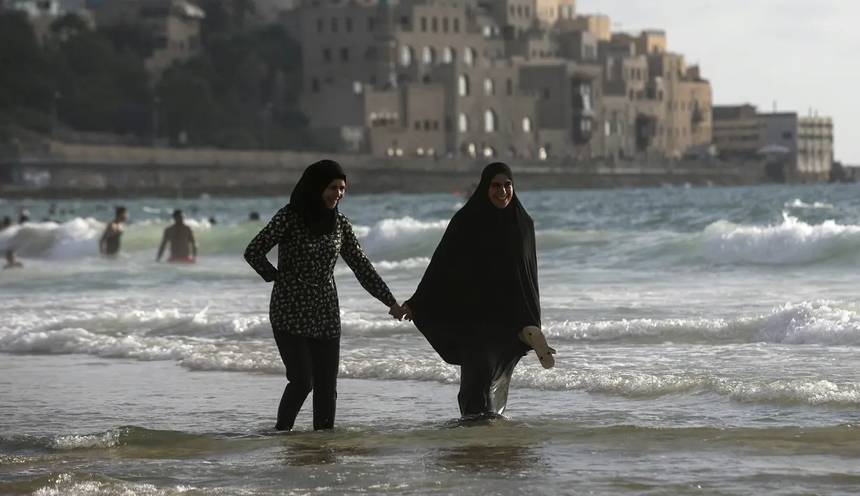 Dua warga Palestina berjalan di pinggir 7/2015). Selama Idul Fitri, pemerintah Israel mengizinkan warga Palestina untuk berwisata di sepanjang garis pantai Mediterania. (REUTERS/Baz Ratner)