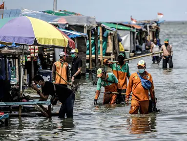 Petugas PPSU membersihkan sampah saat terjadi banjir rob di Pelabuhan Kali Adem, Muara Angke, Jakarta, Selasa (9/11/2021). Walau terendam banjir rob, petugas PPSU tetap sigap bersihkan sampah yang mengambang terbawa air laut. (Liputan6.com/Faizal Fanani)