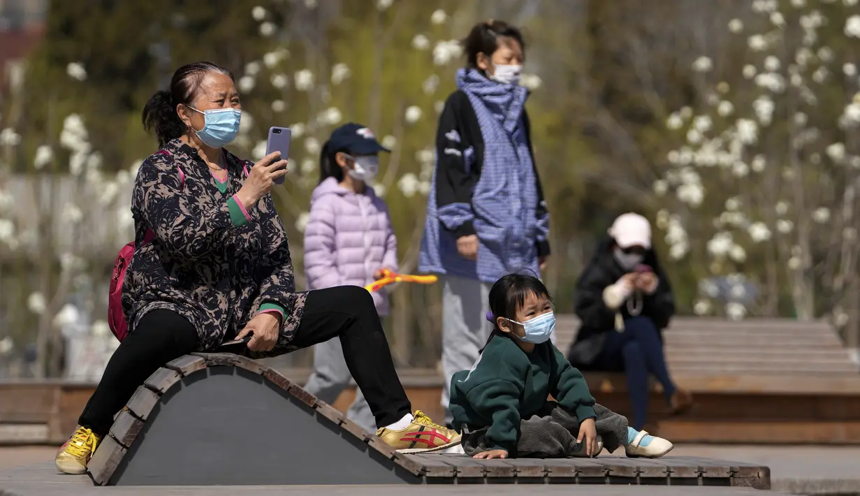 Warga mengenakan masker membawa anak-anak mereka untuk berjemur di luar mal, di Beijing, Minggu (3/4/2022). Kasus COVID-19 di kota terbesar di China, Shanghai, masih meningkat saat jutaan orang tetap terisolasi di rumah di bawah lockdown besar-besaran. (AP Photo/Andy Wong)