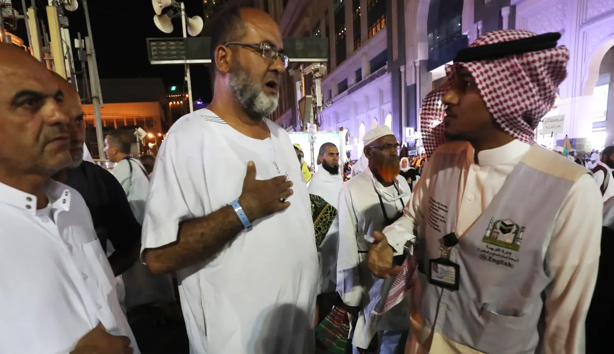 Jemaah haji berbincang dengan seorang penerjemah di kota suci Islam, Makkah, Arab Saudi, 17 Agustus 2018. Para penerjemah ini bisa dicirikan dengan pria yang memakai rompi abu-abu, dan di dadanya dibordir nama bahasa yang dia kuasai. (AFP/AHMAD AL-RUBAYE)