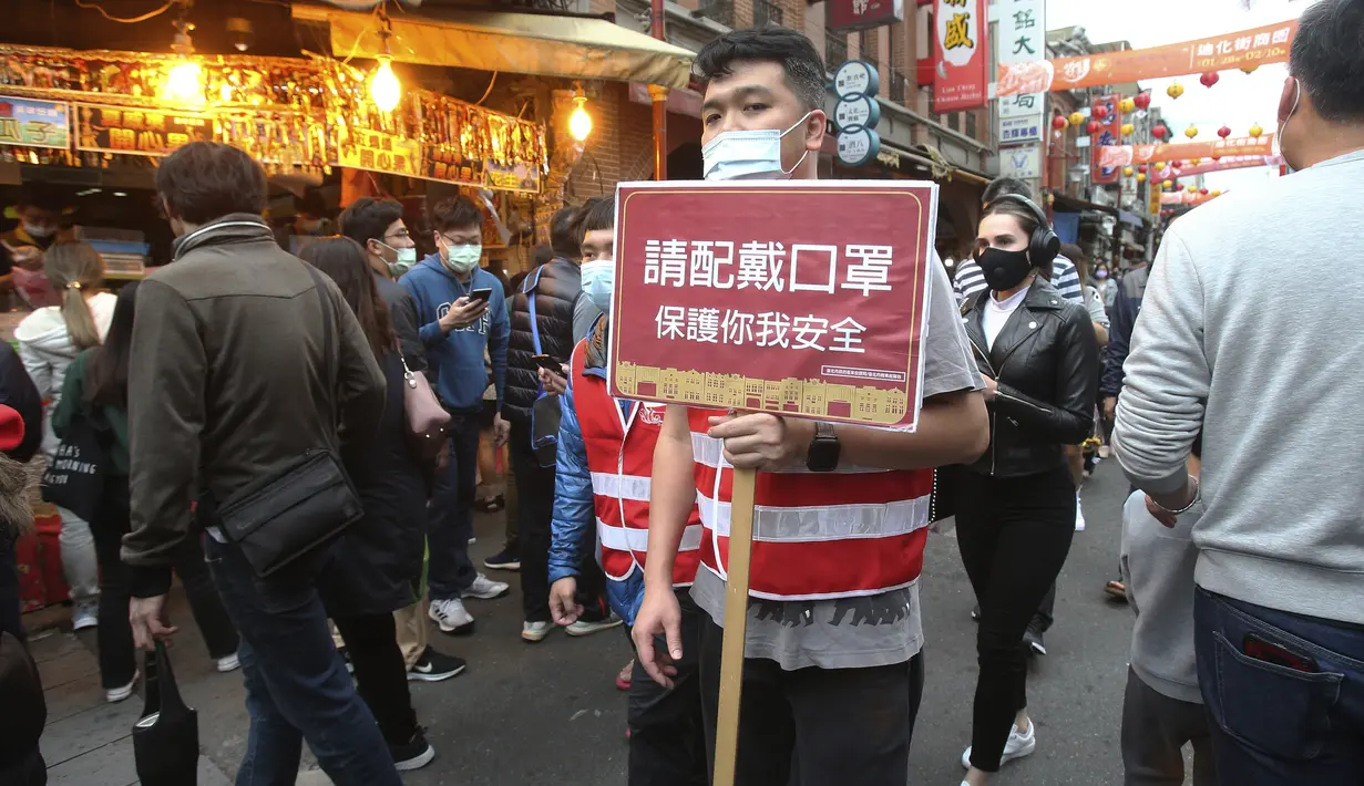 Seorang karyawan memegang tanda bertuliskan "Tolong pakai masker untuk melindungi Anda dan saya." dan berjalan-jalan di antara para pembeli untuk perayaan Tahun Baru Imlek di pasar Dihua Street di Taipei, Taiwan, Rabu (10/2/2021). (AP Photo/Chiang Ying-ying)