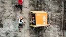 Seorang pemanjat tebing membeli air mineral di toko serba ada yang menempel di dinding tebing di Pingjiang di provinsi Hunan, China (25/4). Toko ini menjual minuman dan makanan untuk para pemanjat tebing yang melintas. (AFP Photo/China Out)