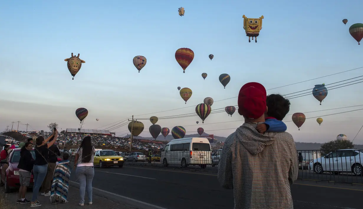 Warga melihat balon udara yang menghiasi langit di Cajititlan, Meksiko, Minggu (7/5).  Festival balon udara ini menjadi tontonan menarik bagi warga sekitar dan wisatawan. (AFP PHOTO / Hector Guerrero)