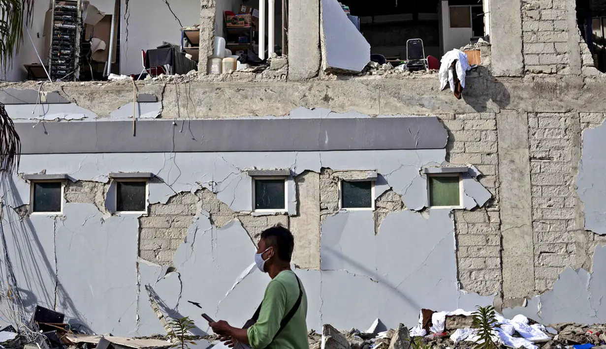 Seorang pria berjalan melewati bangunan yang rusak akibat gempa di Mamuju, Sulawesi Barat, Indonesia, Senin (18/1/2021). Jumlah warga yang mengungsi usai gempa magnitudo 6,2 di Sulawesi Barat mencapai 19.435 orang. (AP Photo/Yusuf Wahil)