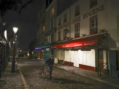 Seorang pria mendorong sepedanya di sepanjang deretan restoran yang tutup selama jam malam di Montmartre, Paris, Perancis, Selasa (15/12/2020). Pemerintah Perancis mencabut kebijakan lockdown terkait COVID-19 dan mulai memberlakukan jam malam. (AP Photo/Michel Euler)