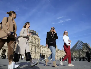 Turis tanpa mengenakan masker berjalan di sebelah Museum Louvre, di Paris, Senin (14/3/2022). Prancis telah mencabut sebagian besar pembatasan COVID-19 pada hari Senin, memungkinkan orang melepas masker di hampir semua tempat. (AP Photo/Francois Mori)