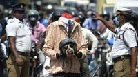 Petugas polisi bersama seorang sukarelawan (tengah) berpakaian seperti pengendara sepeda motor yang memegang kepala mockup dengan helm ambil bagian dalam kampanye kesadaran keselamatan jalan, di Chennai (7/7/2021). (AFP/Arun Sankar)