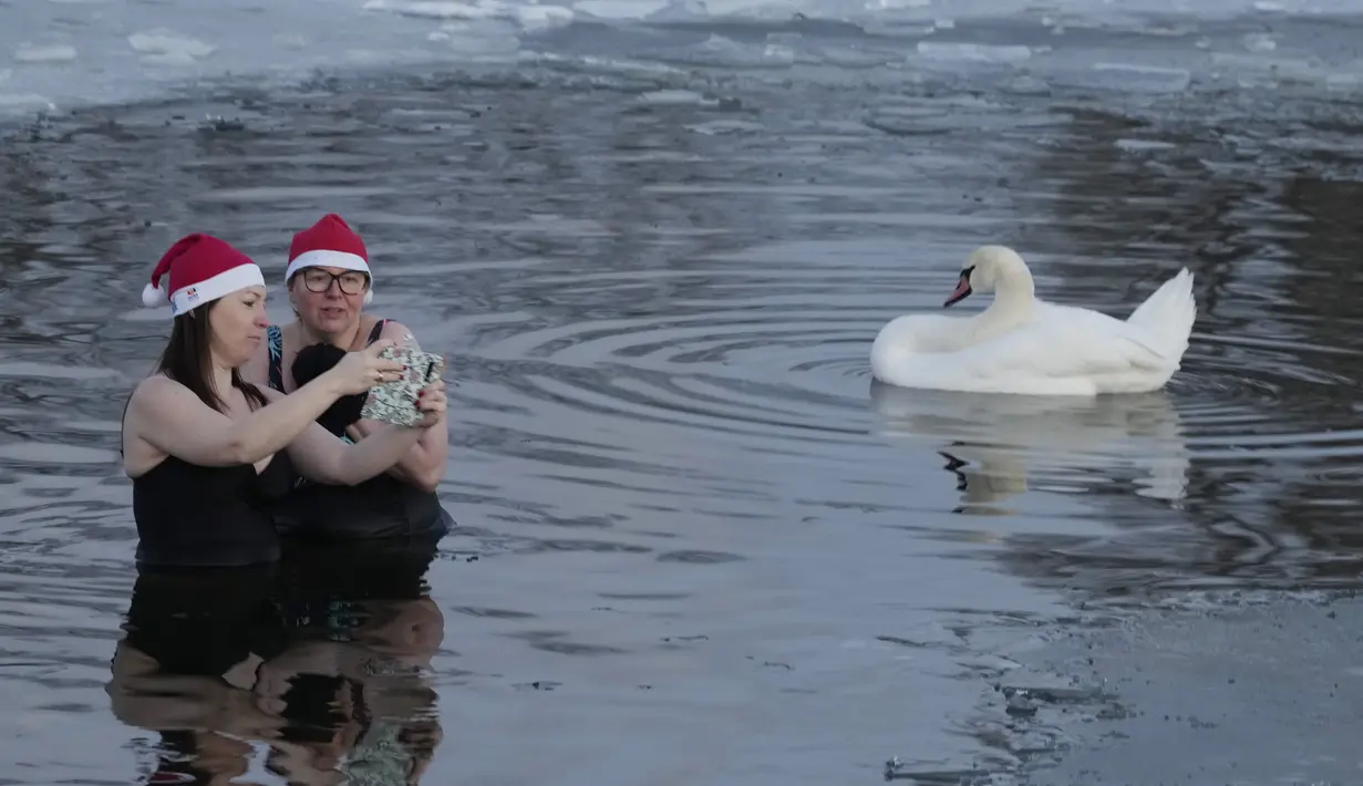 Dua wanita berselfie saat berenang di danau dengan suhu di bawah titik beku di Warsawa, Polandia (26/12/2021). Iklim di Polandia pada musim dingin yang sangat dingin, seringkali di bawah titik beku (0 °C atau 32 °F), dan musim panas yang hangat.  (AP Photo/Czarek Sokolowski)