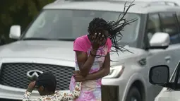 Seorang gadis muda menutupi wajahnya dari angin dan hujan yang dihasilkan oleh Badai Ida di New Orleans, Minggu (29/8/2021).  Badai level 4 itu memanjang hingga sejauh 50 mil dari episentrumnya. (AP Photo/Eric Gay)