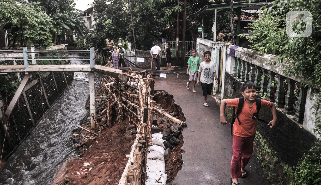 Anak-anak melintas di dekat lokasi turap longsor di Batu Ampar, Kramat Jati, Jakarta, Selasa (23/2/2021). Beruntung tidak ada korban jiwa dalam kejadian ini namun warga setempat terpaksa menutup akses jalan di sekitar lokasi guna mencegah longsor susulan.  (merdeka.com/Iqbal S. Nugroho)