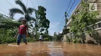 Anak-anak melintasi banjir di Perumahan Bumi Nasio Indah, Bekasi, Jawa Barat, Selasa (2/11/2021). Hingga saat ini, petugas masih memeriksa kondisi tanggul yang jebol sejak Senin sore kemarin. (Liputan6.com/Herman Zakharia)