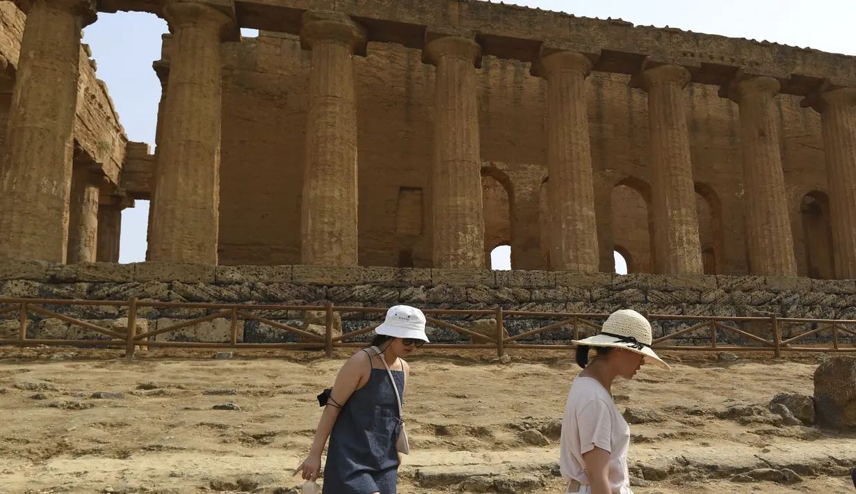 Dua wanita berjalan saat mengunjungi Lembah Kuil selama gelombang panas di dekat Agrigento, Sisilia, Italia (11/8/2021). Gelombang panas yang berkelanjutan akan berlangsung hingga akhir pekan dengan suhu diperkirakan mencapai lebih dari 40 derajat Celcius di banyak bagian dari Italia. (AP Photo/Salv