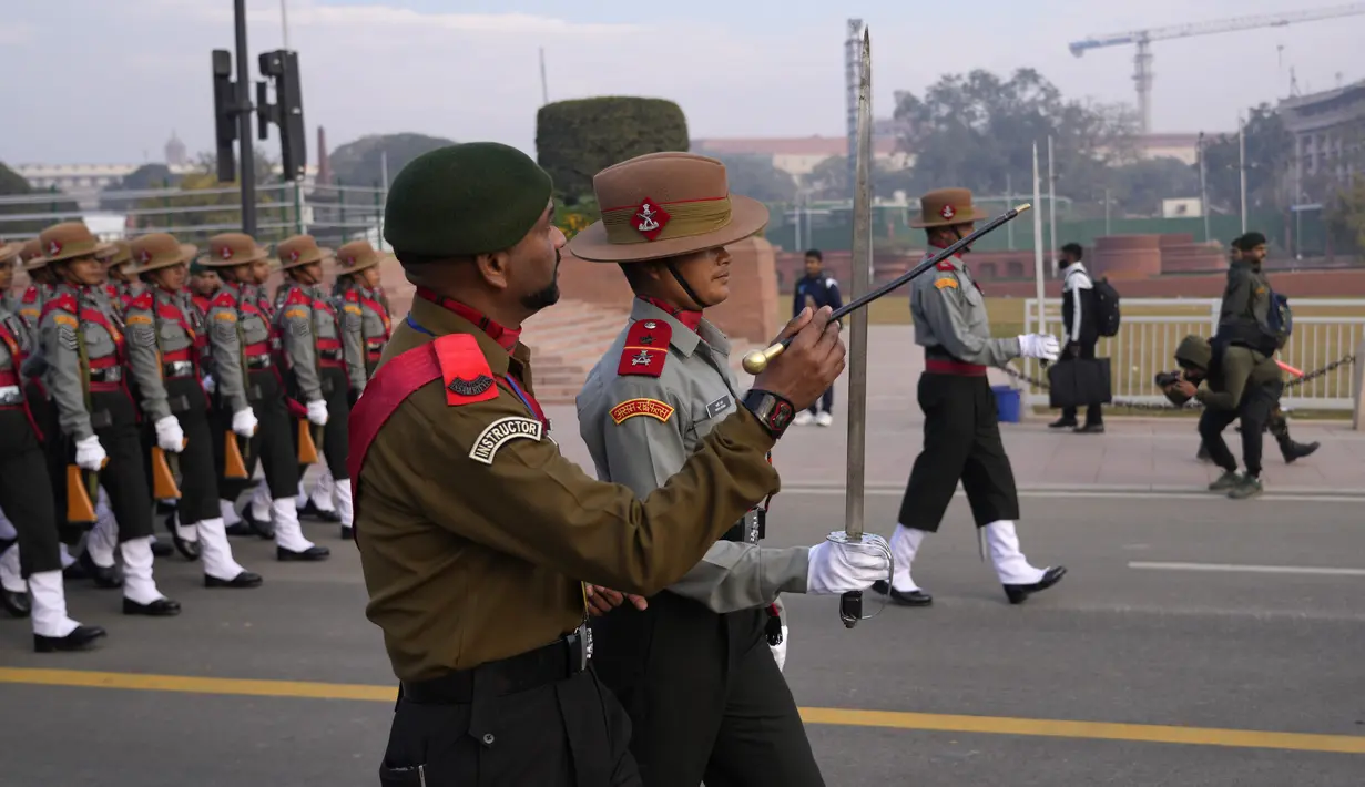 Seorang instruktur Assam Rifles, pasukan paramiliter India, mengoreksi posisi pedang seorang tentara, memimpin kontingen, saat mereka berlatih pawai untuk parade hari Republik mendatang di perbukitan Raisina, di New Delhi, India, Kamis (19/1/2023). Untuk memperingatinya setiap tahun diselenggarakan parade militer di New Delhi. (AP Photo/Manish Swarup)