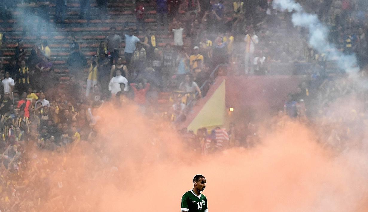 Pemain Arab Saudi, Yasyn Alnakhli, melintas diantara suar yang dinyalakan suporter Malaysia pada laga Pra Piala Dunia 2018 di Malaysia, Selasa (8/9/2015). (AFP Photo/Manan Vatsyayana)