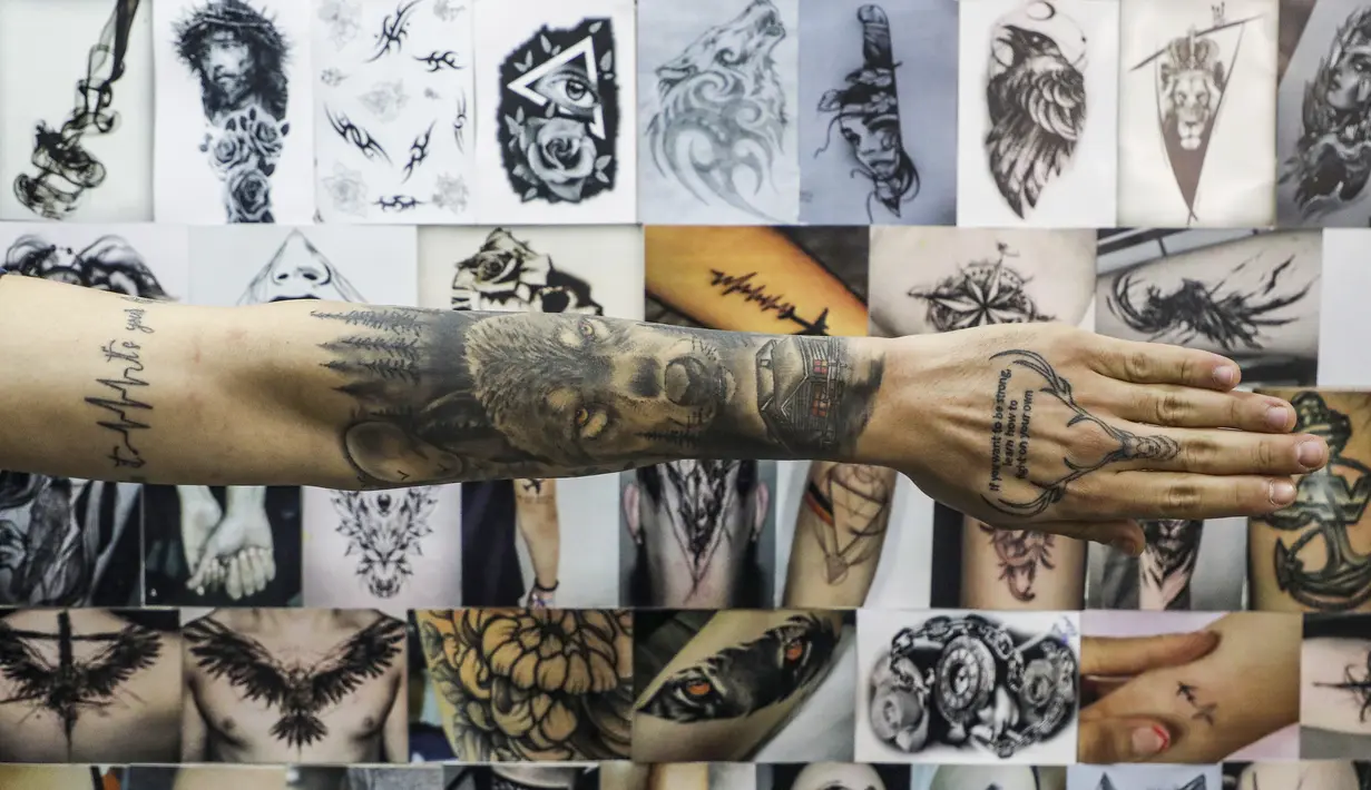 Klien Naim Abdallah memamerkan tato baru di lengan dan tangannya di samping dinding yang menampilkan ilustrasi karya dan desain tatto Naim Abdallah di ruang tamu di Kota Betlehem di Tepi Barat (24/1/2021). (AFP/Hazem Bader)