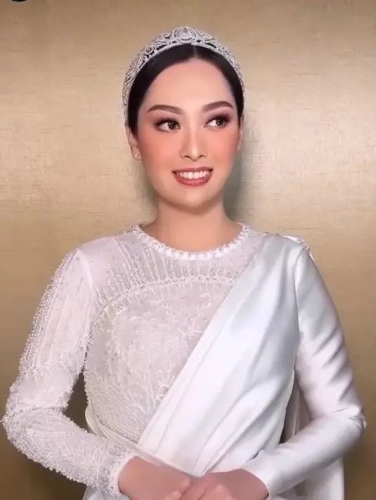 Sementara di acara resepsi, Rizka memilih tampilan klasik dengan gaun kombinasi satin dan brokat warna putih. Penampilannya juga dilengkapi tiara yang cantik.
