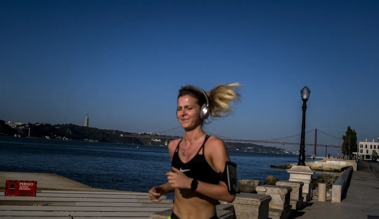 Seorang pelari berlari melewati Ribeira das Naus di Lisbon (14/7/2021). Hampir setengah dari populasi Portugal diberlakukan jam malam lagi awal bulan ini. (AFP/Patricia De Melo Moreira)