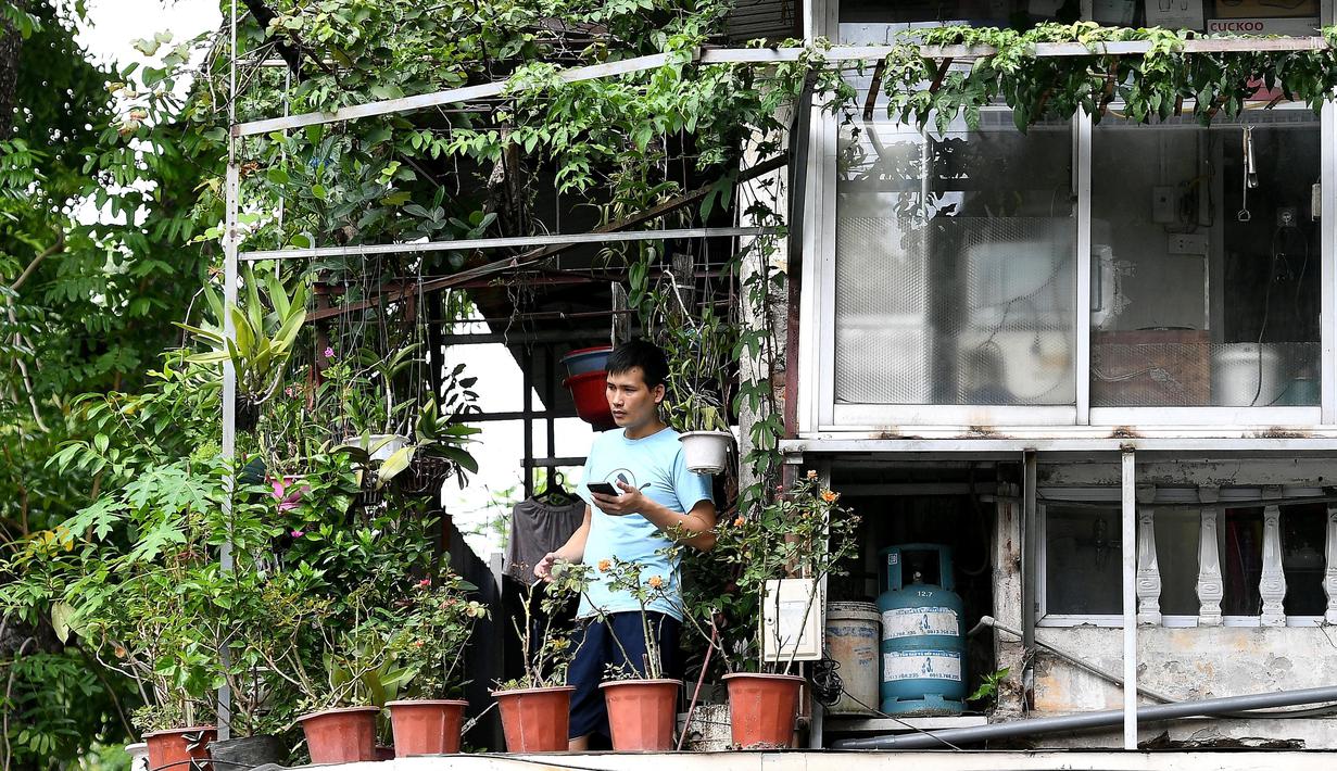 Gambar pada 4 September 2021 menunjukkan seorang pria memeriksa ponselnya sambil berdiri di balkon rumahnya di Hanoi, Vietnam, selama lockdown Covid-19. Menghadap ke jalan yang sepi, balkon kecil mereka menjadi saksi bisu terkait aktivitas yang dilakukan oleh masing-masing keluarga (Nhac NGUYEN/AFP)