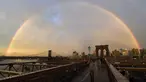 Pejalan kaki melintasi Jembatan Brooklyn saat pelangi menghiasi langit New York City, AS (15/5). Jembatan Brooklyn adalah salah satu jembatan suspensi tertua di Amerika Serikat. (AFP Photo/Hector Retamal)