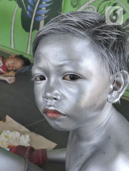 Seorang anak yang mengamen sebagai "Manusia Silver " beristirahat bersama ibunya di salah satu sudut toko di kawasan perempatan Gaplek, Pamulang, Tangerang Selatan, Sabtu (16/1/2021). Keluarga tersebut mendapat penghasilan sekitar 50 ribu per hari sebagai Manusia Silver . (merdeka.com/Arie Basuki)