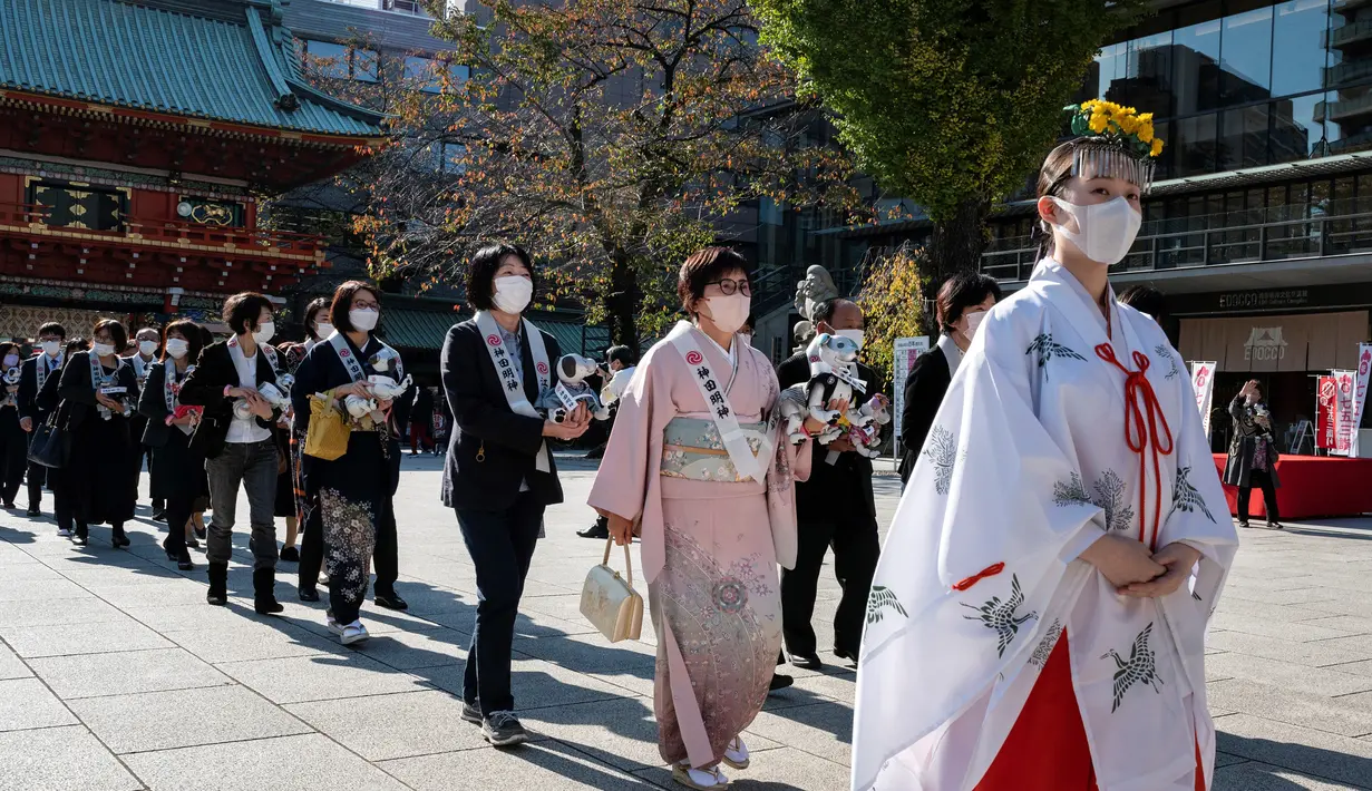 Pemilik robot anjing "aibo" mengikuti seorang gadis kuil (kanan) saat mereka melanjutkan ke aula kuil untuk menandai Festival Shichi-Go-San di Kuil Kanda Myojin, Tokyo, Jepang, Jumat (11/11/2022). Lebih dari 60 pemilik "aibo" menghadiri acara tradisional yang diadakan setiap tahun dengan mendoakan kesehatan yang baik di masa depan untuk anak perempuan berusia tiga dan tujuh tahun dan anak laki-laki berusia lima tahun. (Richard A. Brooks / AFP)