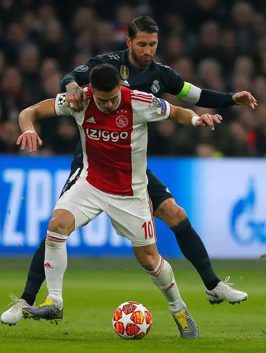 Pemain Ajax Dusan Tadic berebut bola dengan bek Real Madrid, Sergio Ramos pada leg pertama 16 besar Liga Champions di Johan Cruijff ArenA, Amsterdam, Rabu (13/2). Real Madrid harus bersusah payah menaklukkan Ajax dengan skor tipis 2-1. (AP/Peter Dejong)