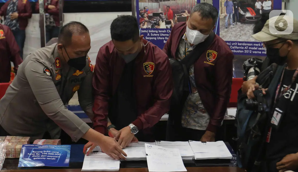 Petugas polisi menata barang bukti saat jumpa pers kasus Binomo dengan tersangka Indra Kesuma alias Indra Kenz di Mabes Polri, Jakarta, Jumat (25/3/2022). Hingga kini, pihak berwajib masih menelusuri terkait aset lain yang diduga masih disembunyikan oleh Indra Kenz. (Liputan6.com/Herman Zakharia)