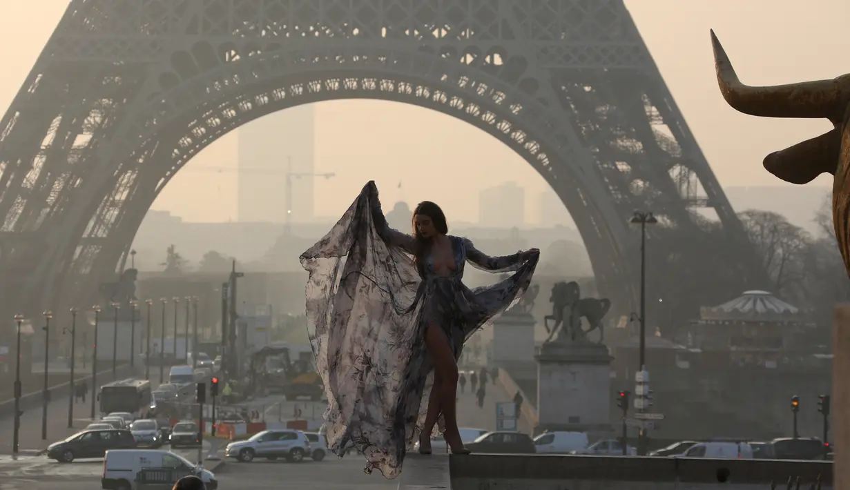 Model seksi ini bergaya di depan menara Eiffel saat matahari terbit dalam sesi pemotretan, Paris (11/3/2016). (AFP/Ludovic MARIN)