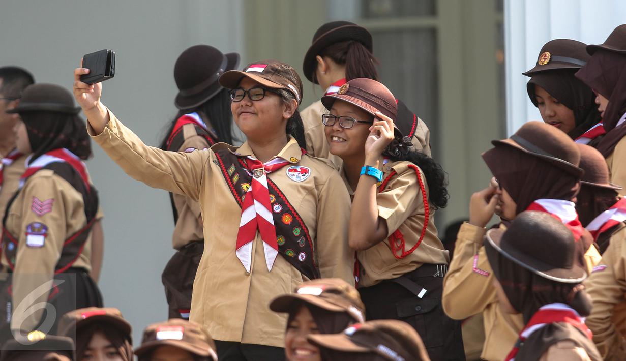 Seorang wanita dari delegasi gerakan Pramuka Indonesia tampak berselfie ria di Halaman Istana Merdeka, Jakarta, Jumat (24/7/2015). 462 kontingen Pramuka Indonesia yang akan mengikuti Jambore Pramuka Dunia ke-23. (Liputan6.com/Faizal Fanani)c