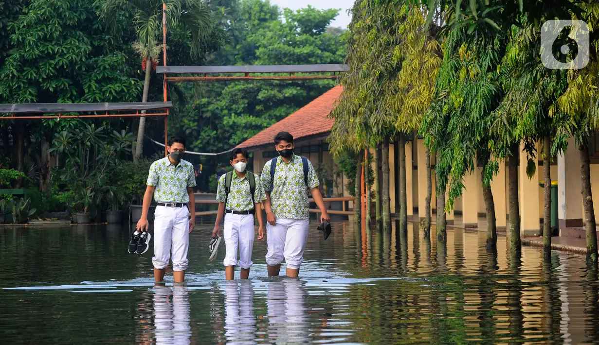 Siswa berjalan melewati banjir yang menggenangi halaman  sekolah di SMAN 4 Tangsel, Pondok Ranji, Tangerang Selatan, Banten, Selasa (14/6/2022). Tiga  pekan lebih banjir merendam lapangan sekolah itu dikarenakan tertutupnya saluran air oleh sampah yang berasal dari tempat pembuangan sampah (TPS) ilegal. (merdeka.com/Arie Basuki)