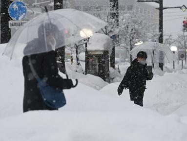 Orang-orang berjalan di atas salju yang menumpuk di depan stasiun kereta Toyama di Toyama, di pantai Laut Jepang, Senin (11/1/2021). Badai musim dingin yang dahsyat menghantam kawasan pesisir di sepanjang Laut Jepang. (Kyodo News via AP)