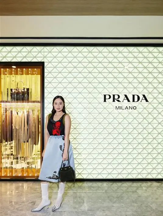 Tatjana Saphira terlihat menarik dengan black patterned sleeveless top yang dipadukan dengan light blue printed midi skirt. Look ini kita maksimal dengan padanan white heeled boots dari Prada. / Foto dok: Prada.